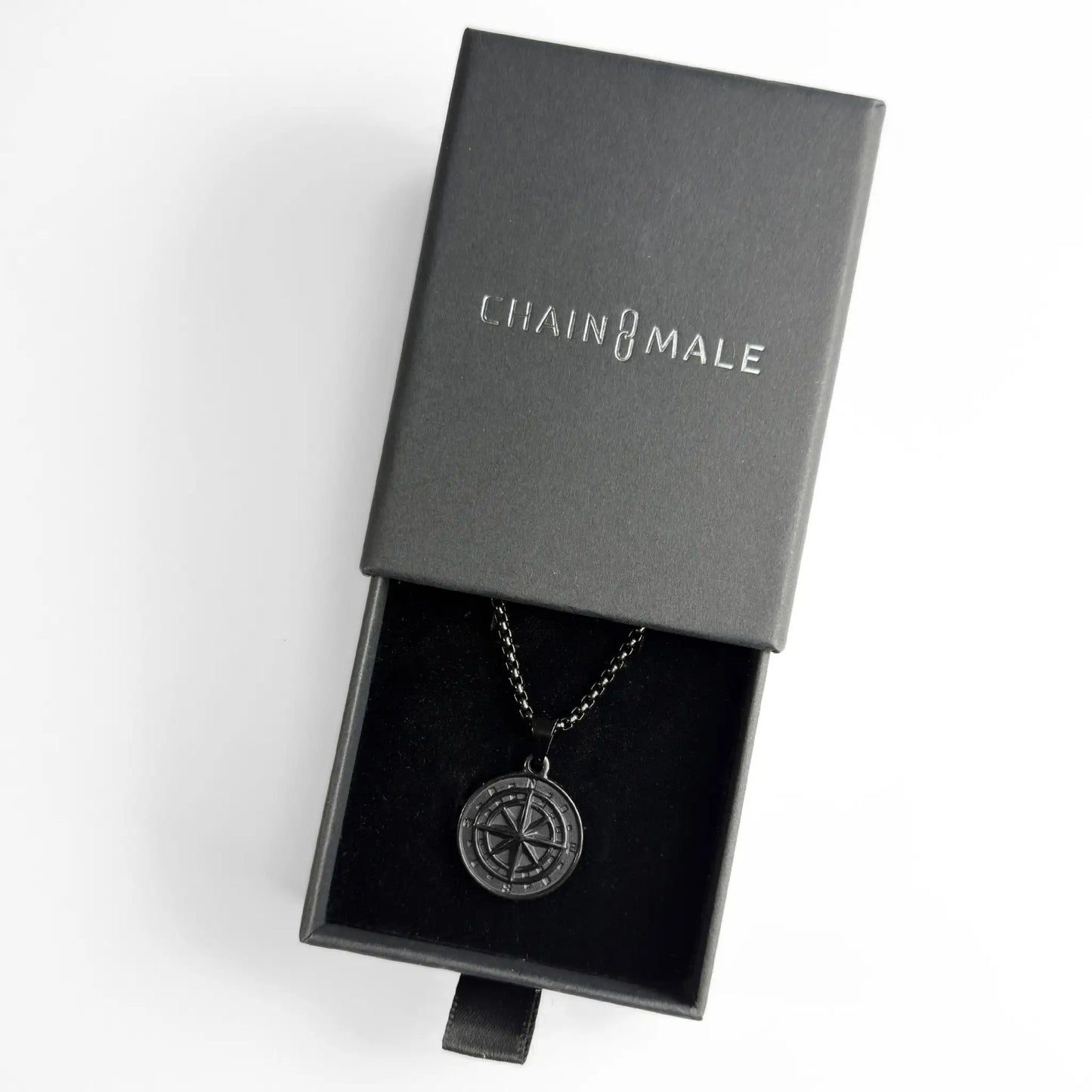 Black compass pendant necklace in a black Chain Male jewellery box against a white background