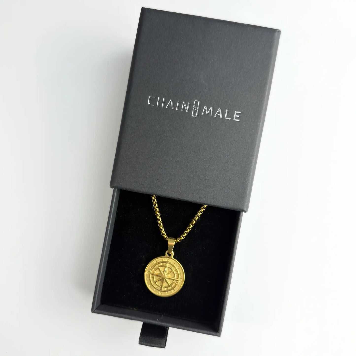 Gold compass pendant necklace in a black Chain Male jewellery box on a white background