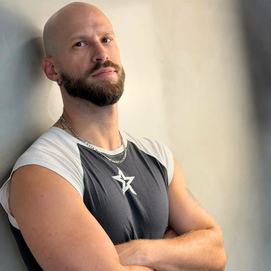 Tattooed bald man wearing a silver 5mm figaro chain necklace with arms crossed in a star print tee