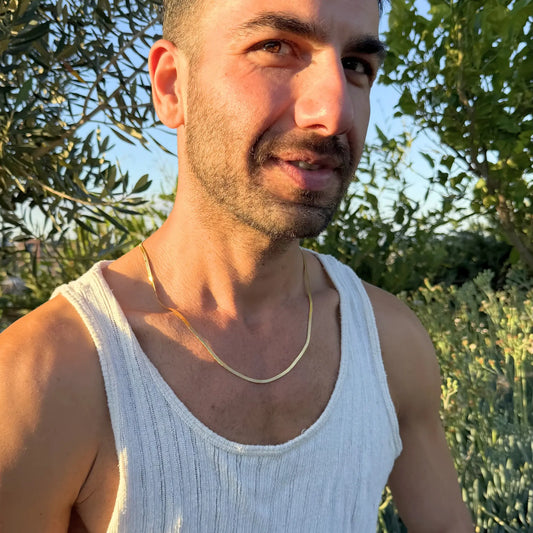 Man wearing a gold 3mm snake chain necklace in a white singlet outdoors, smiling at golden hour
