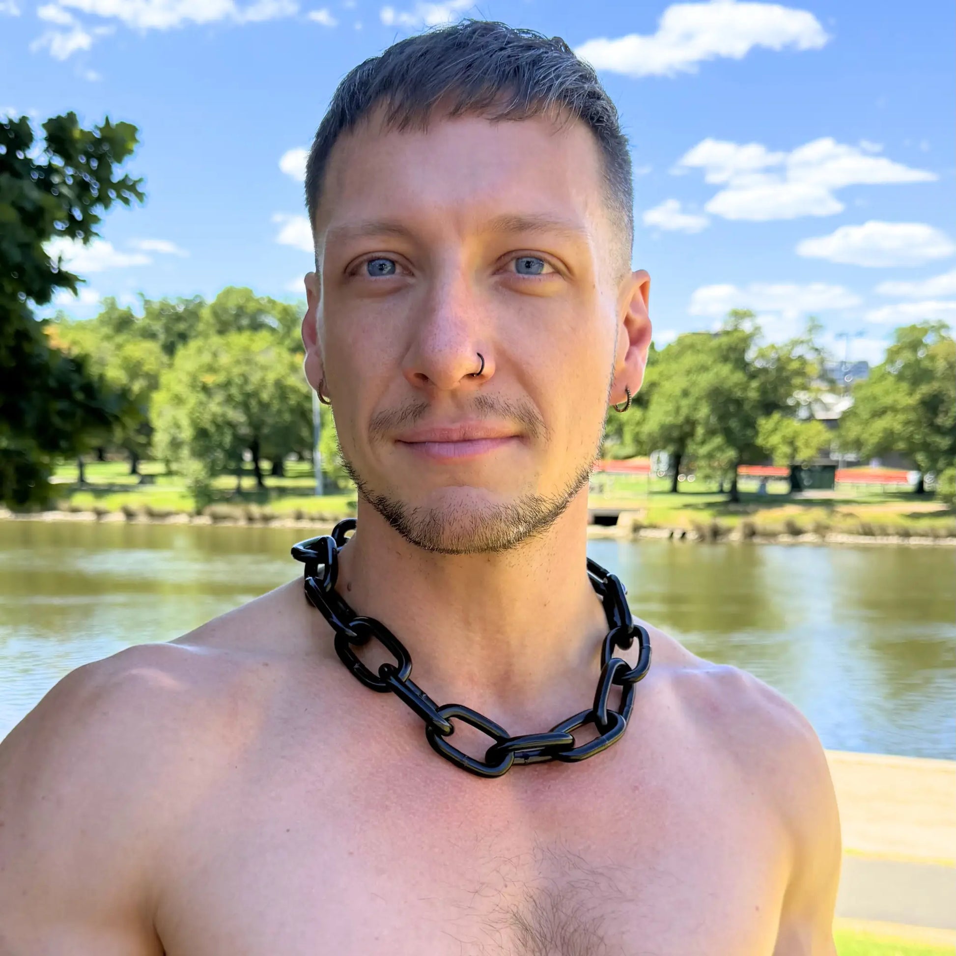Man wearing a Big Black Chain Extra Thick necklace on a bare chest outdoors with park and lake in background