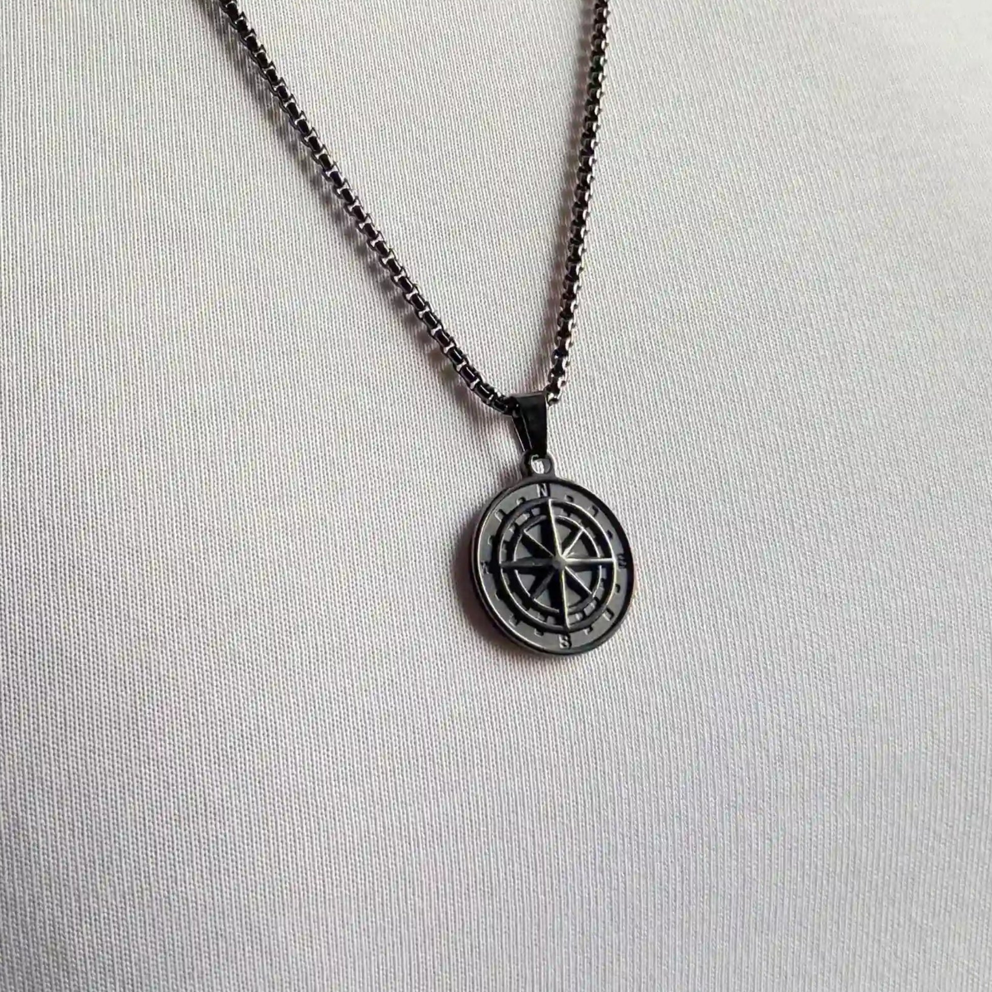 Close up of a black compass pendant necklace worn over a white tshirt