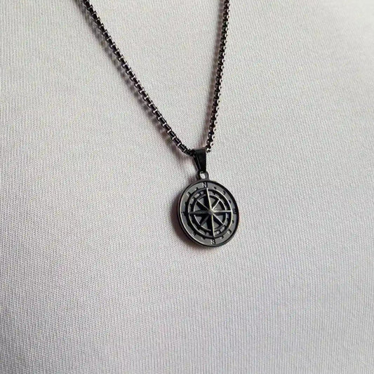 Close up of a black compass pendant necklace worn over a white tshirt