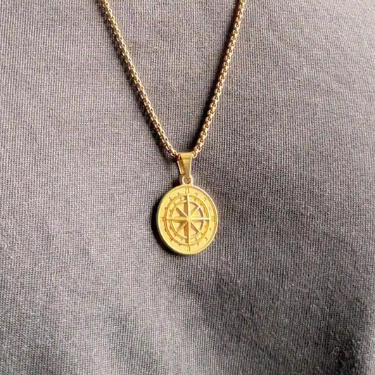 Close up of a gold compass pendant necklace worn over a black tshirt