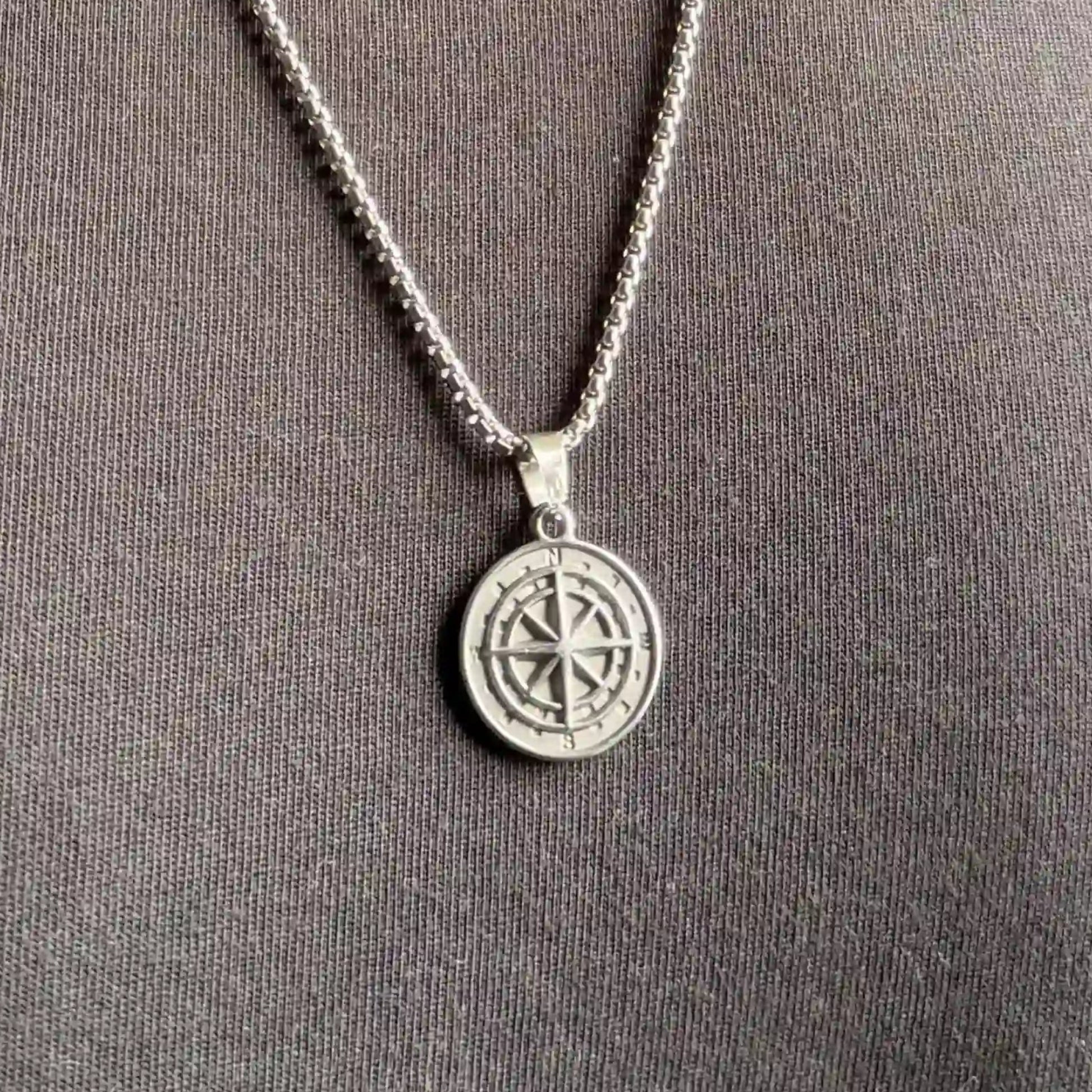 Close up of a silver compass pendant necklace worn over a black tshirt