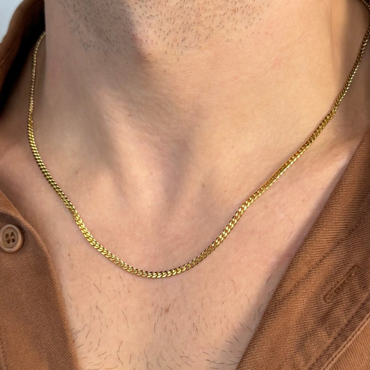 Close-up of a gold 3mm curb chain necklace worn by a man in a brown shirt