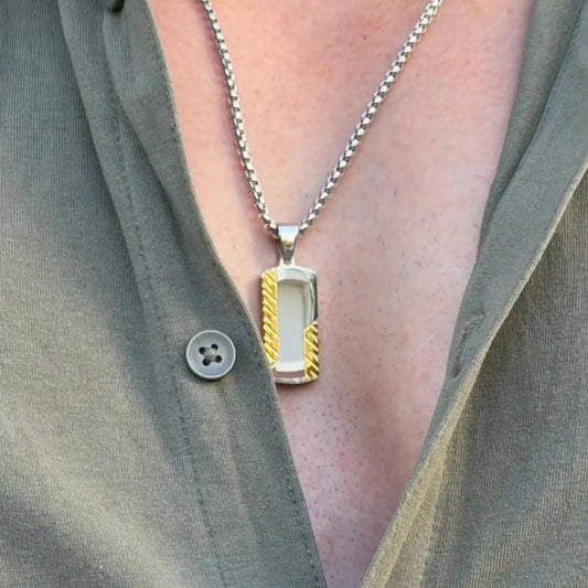 Close up of a gold and silver stainless steel dog tag pendant necklace worn by a man with a casual green button up shirt