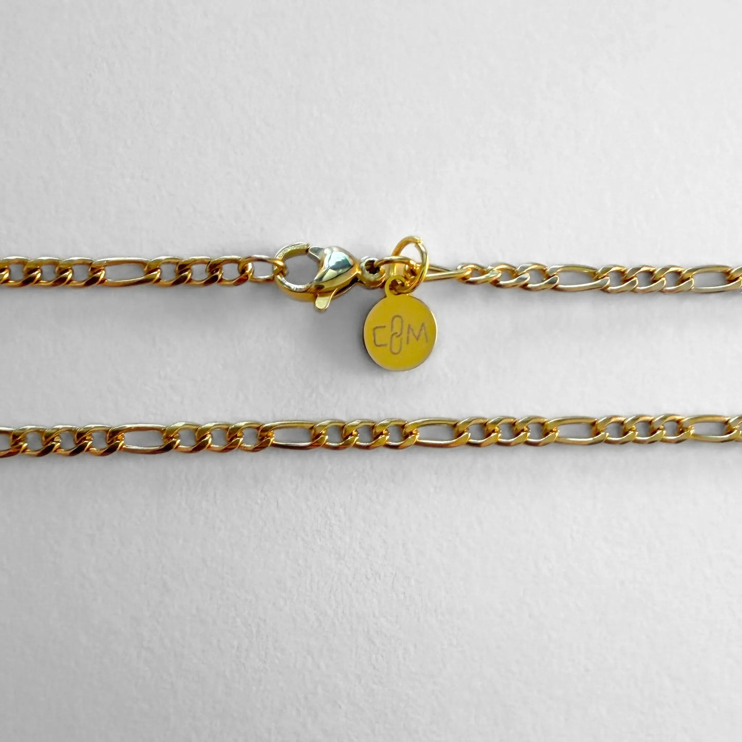 Chain Male gold 3mm Figaro chain necklace flat lay with CM charm, 18ct gold plated men's Everyday collection
