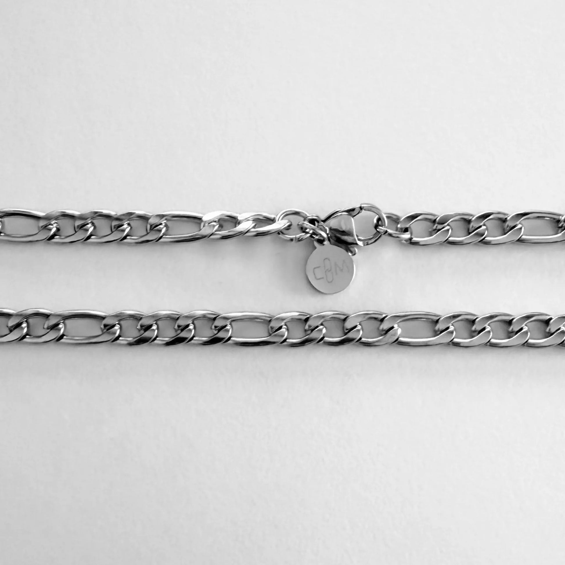 Chain Male silver 5mm Figaro chain necklace flat lay with CM charm, stainless steel men's Everyday collection