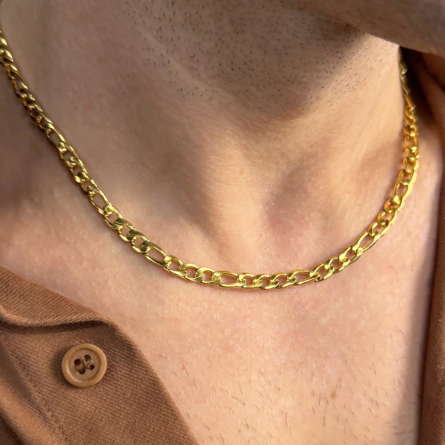 Close-up of a gold 5mm figaro chain necklace worn by a man in a brown shirt