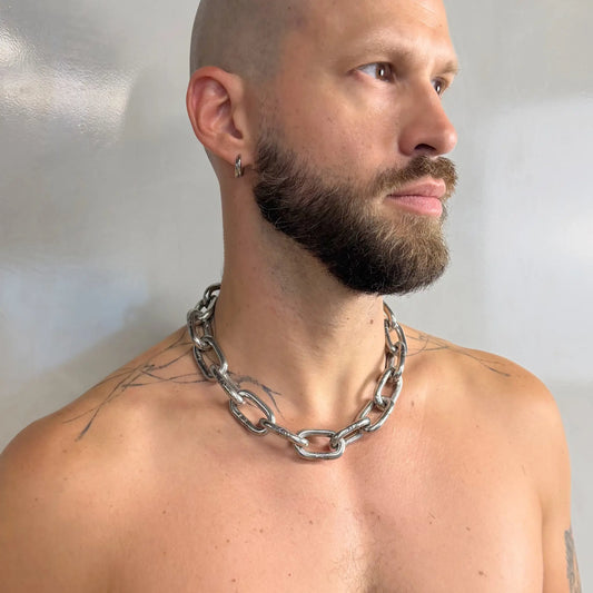 Tattooed bald man wearing a heavy duty stainless steel chain necklace on a bare chest, side profile