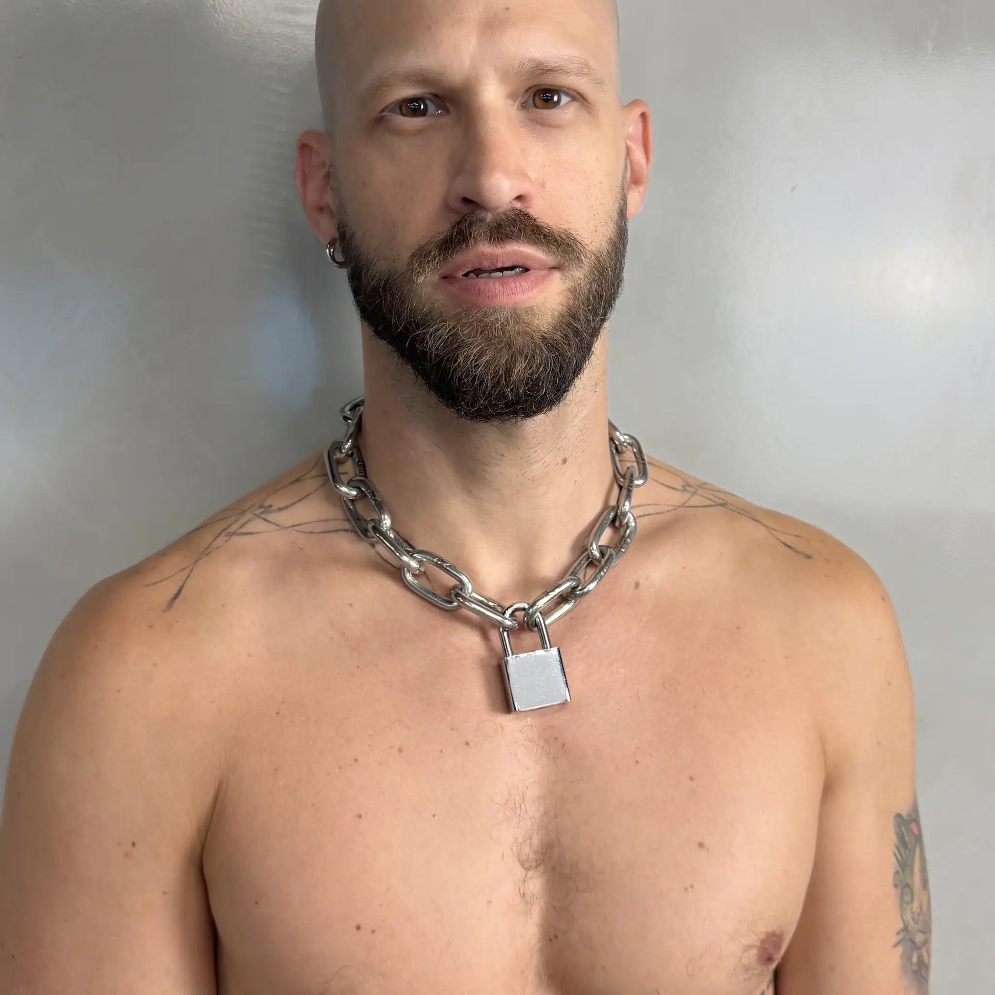 Tattooed bald man wearing a heavy duty stainless steel padlock chain necklace smiling on a bare chest