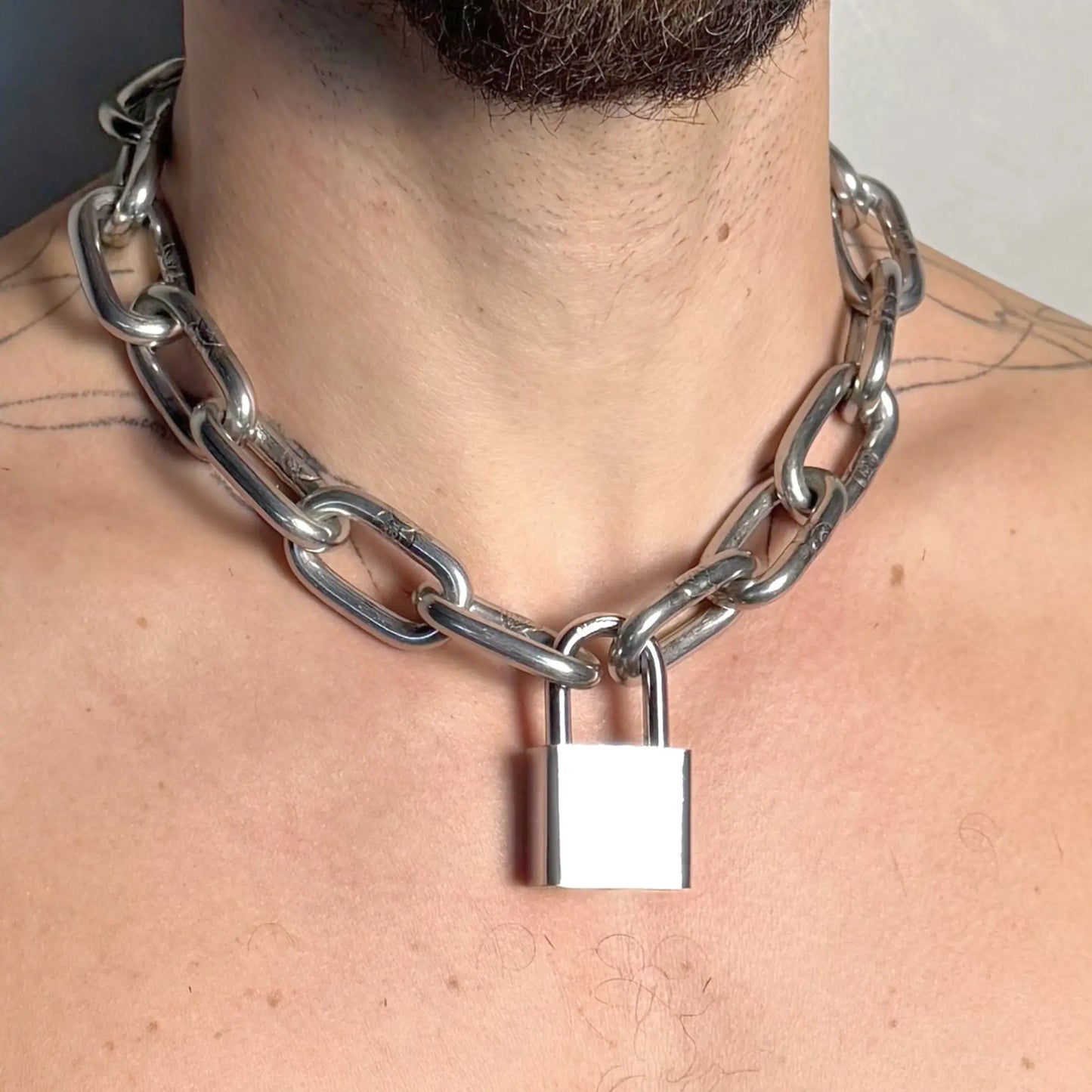 Close-up of a heavy duty stainless steel padlock chain necklace on a tattooed bare chest
