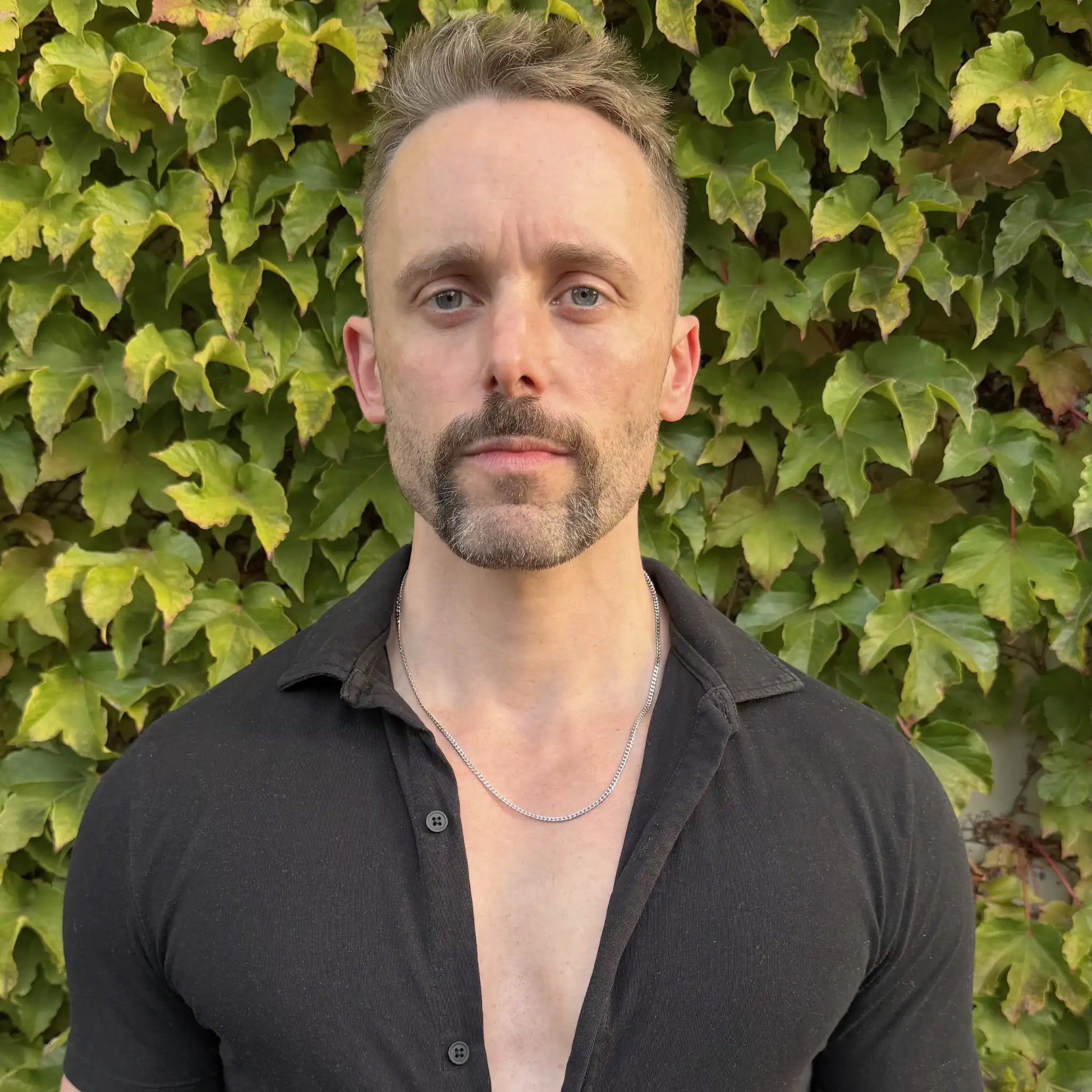 Chain Male silver 3mm curb chain necklace worn on a bearded man with a black shirt against a hedge