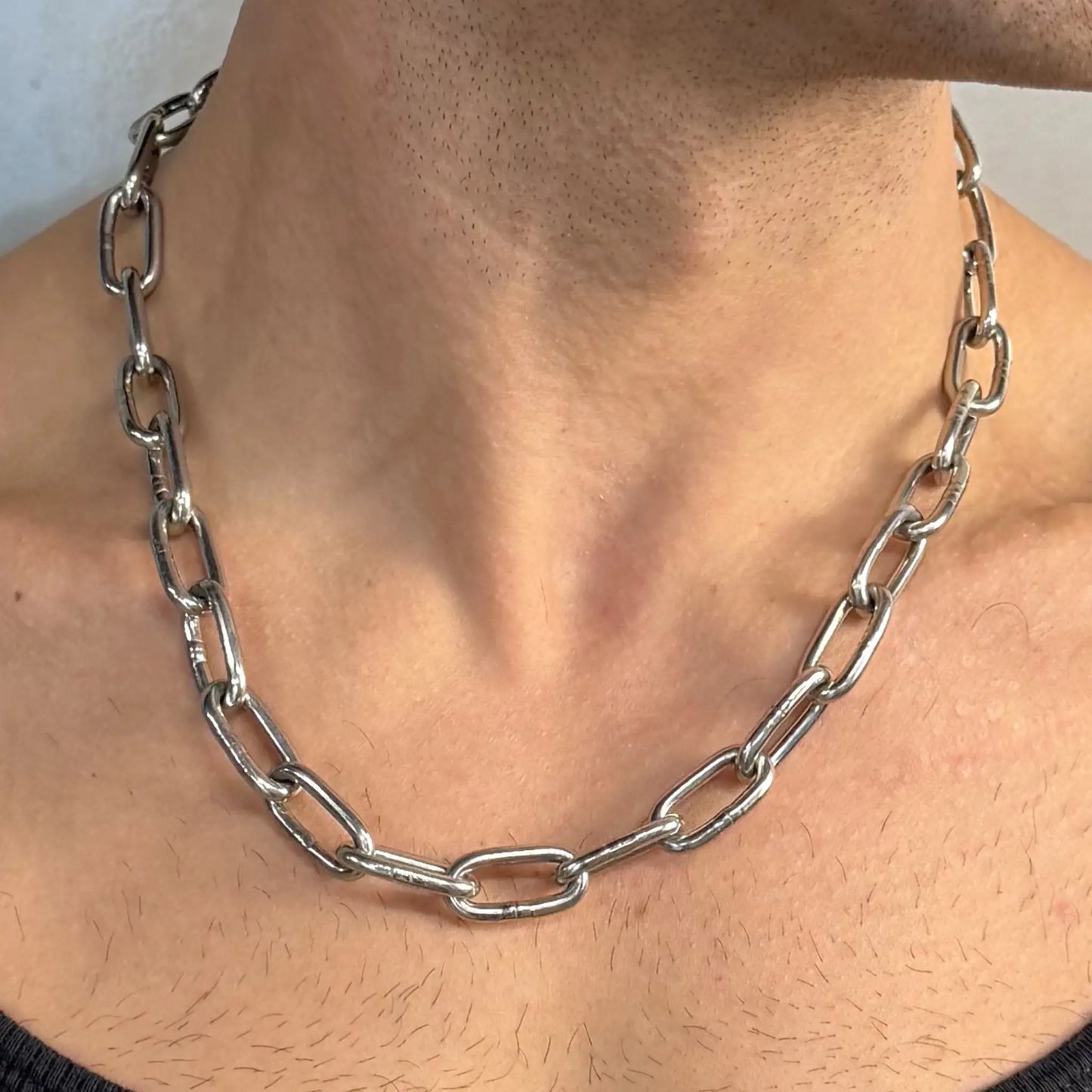 Close-up of a light duty stainless steel chain necklace worn on a bare chest in a black singlet