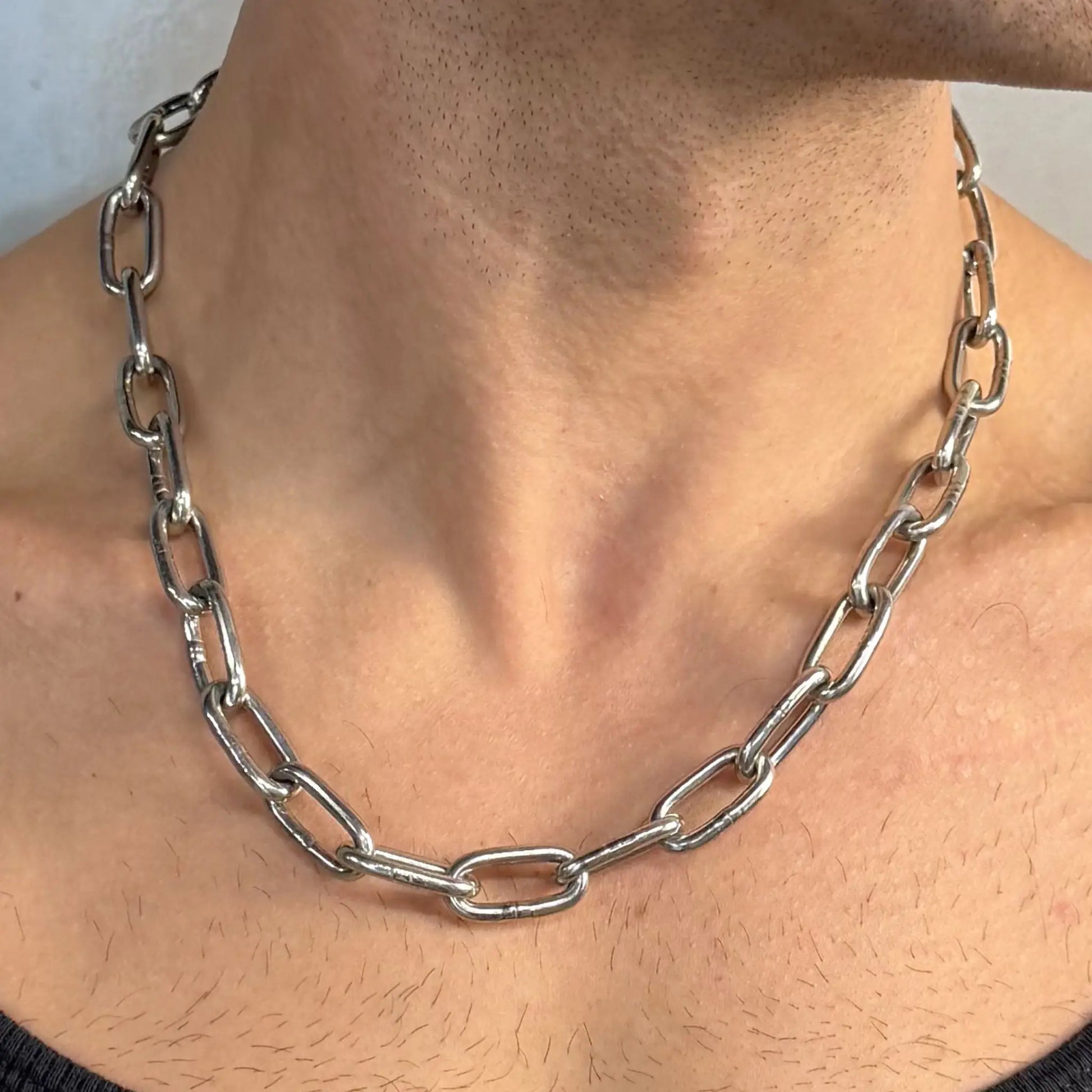 Close-up of a light duty stainless steel chain necklace worn on a bare chest in a black singlet