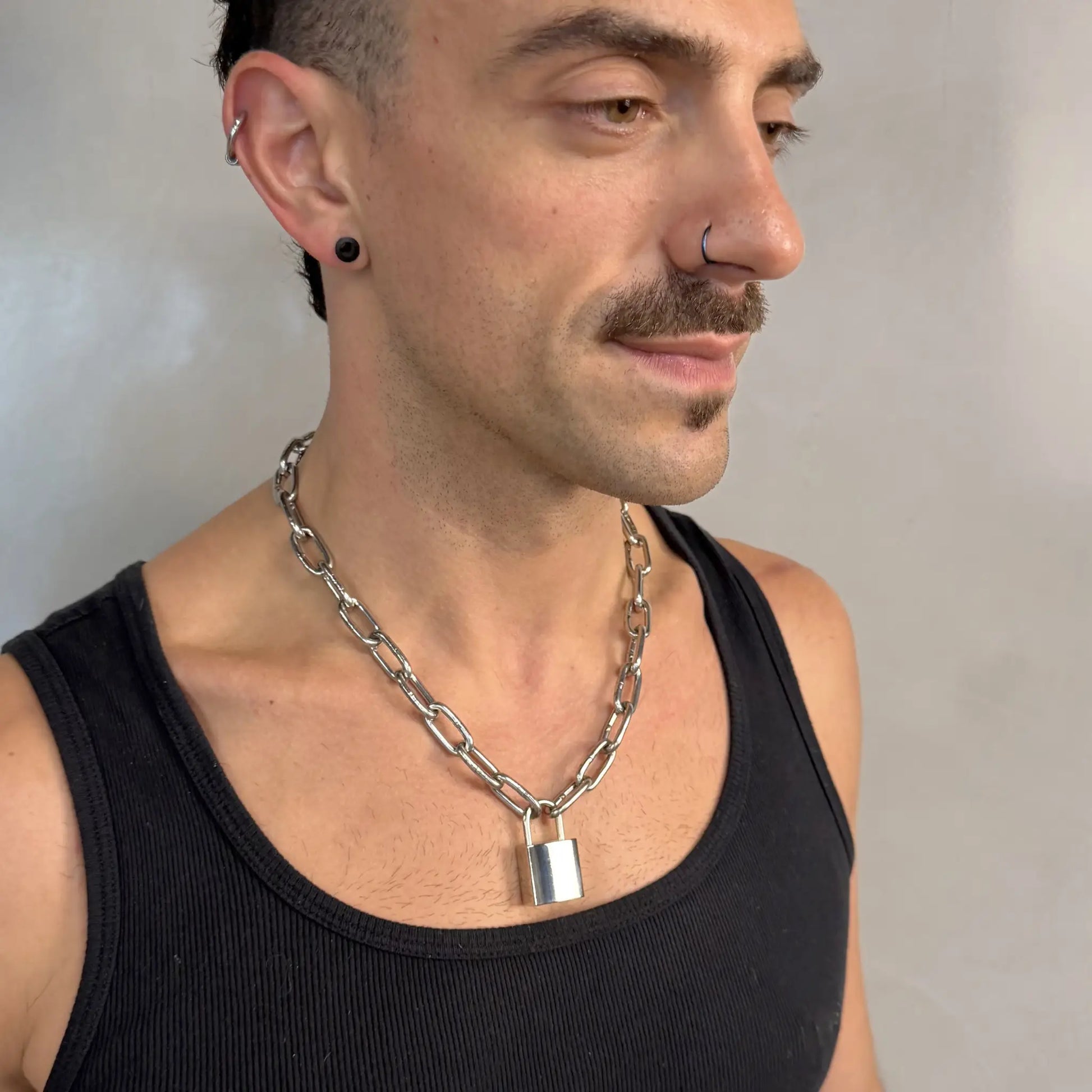 Man wearing a light duty stainless steel padlock chain necklace in a black singlet, side profile with piercings