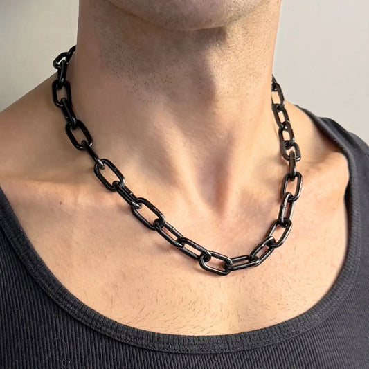 Close-up of a midnight black chain necklace worn on a bare chest in a dark singlet