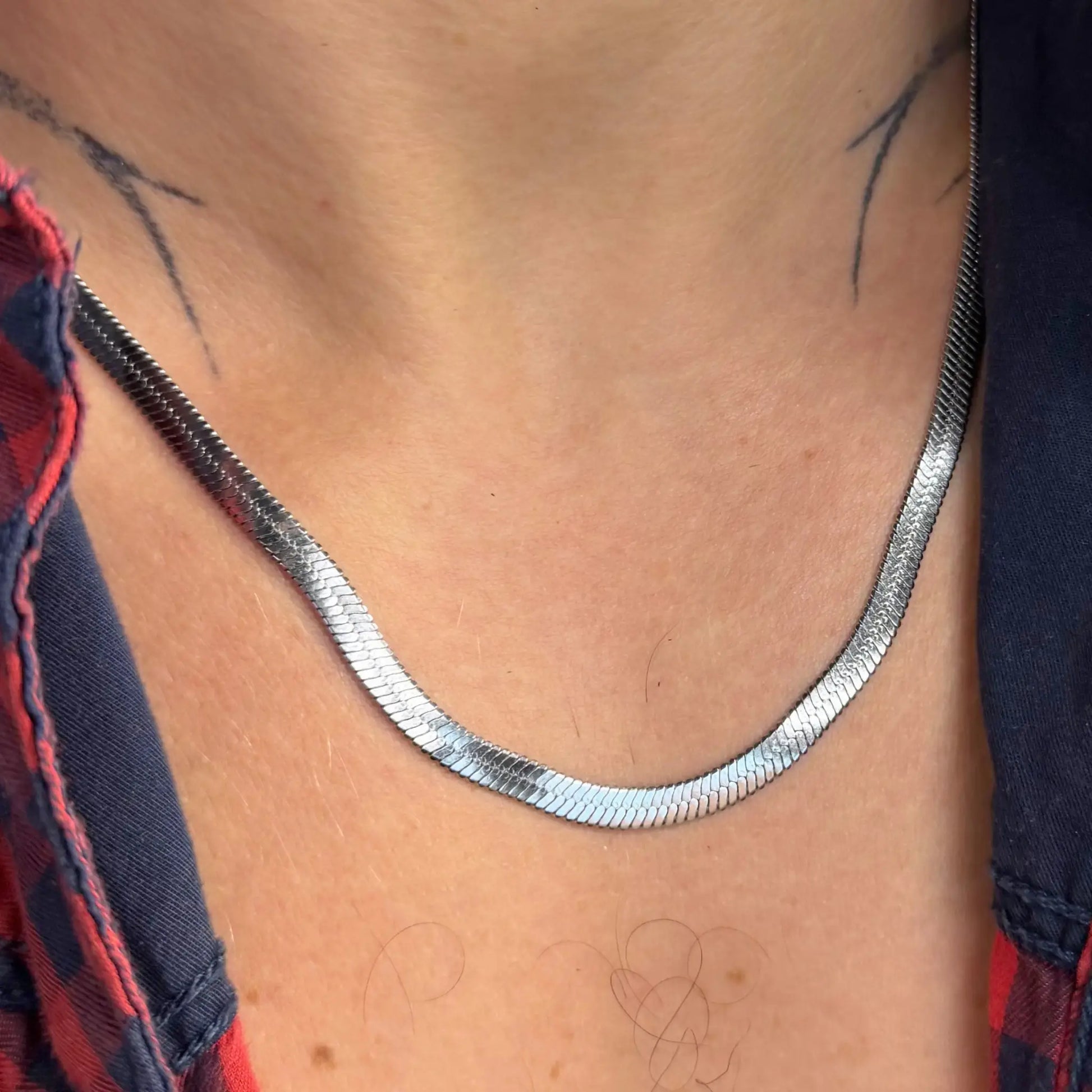 Close-up of a silver 5mm snake chain necklace on a tattooed chest in an open red flannel shirt