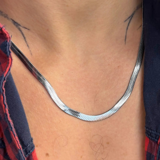 Close-up of a silver 5mm snake chain necklace on a tattooed chest in an open red flannel shirt