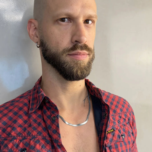 Tattooed bald man wearing a silver 5mm snake chain necklace in an open red flannel shirt facing camera