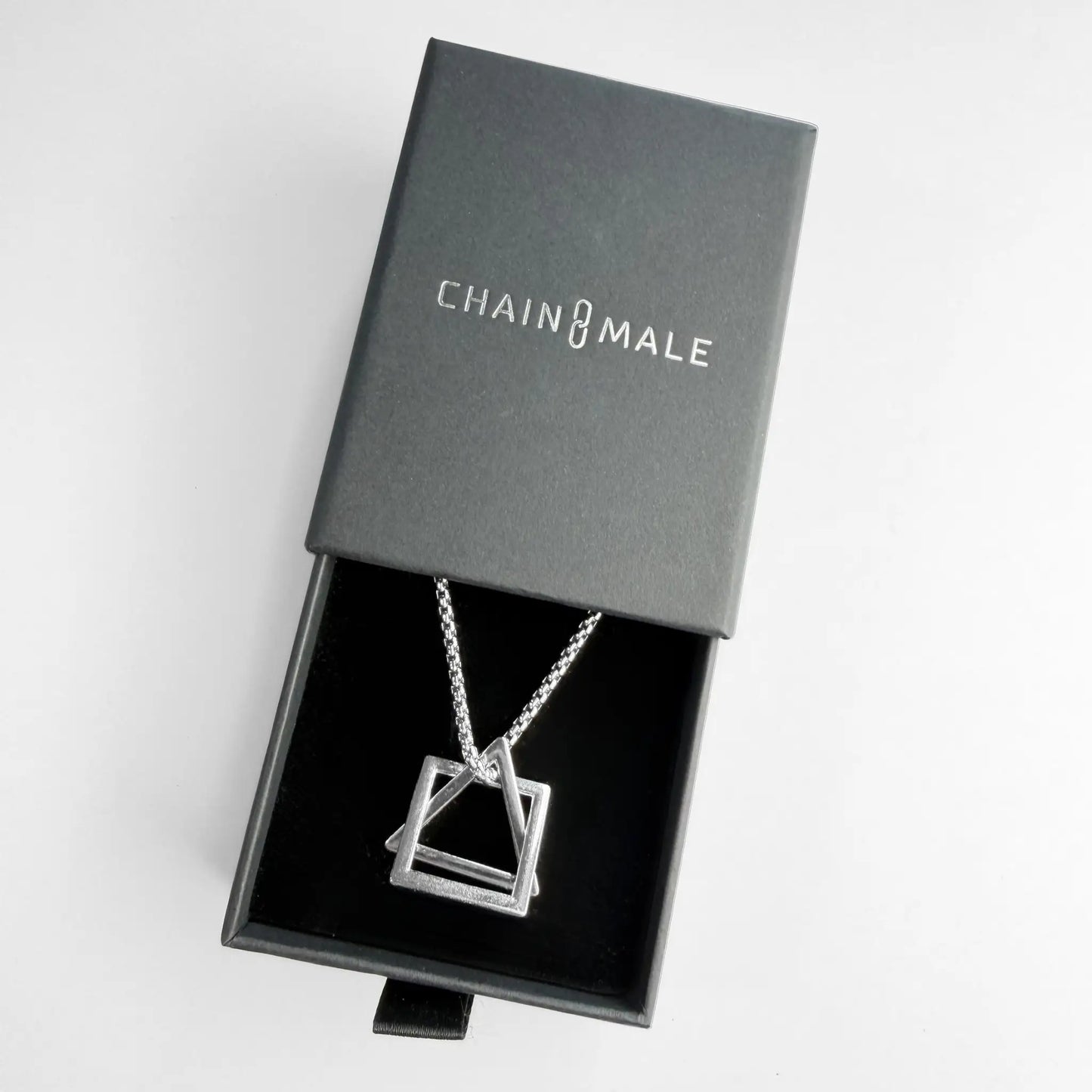 Stainless steel pendant necklace with interlocking square and triangle in a black Chain Male jewellery box on a white background
