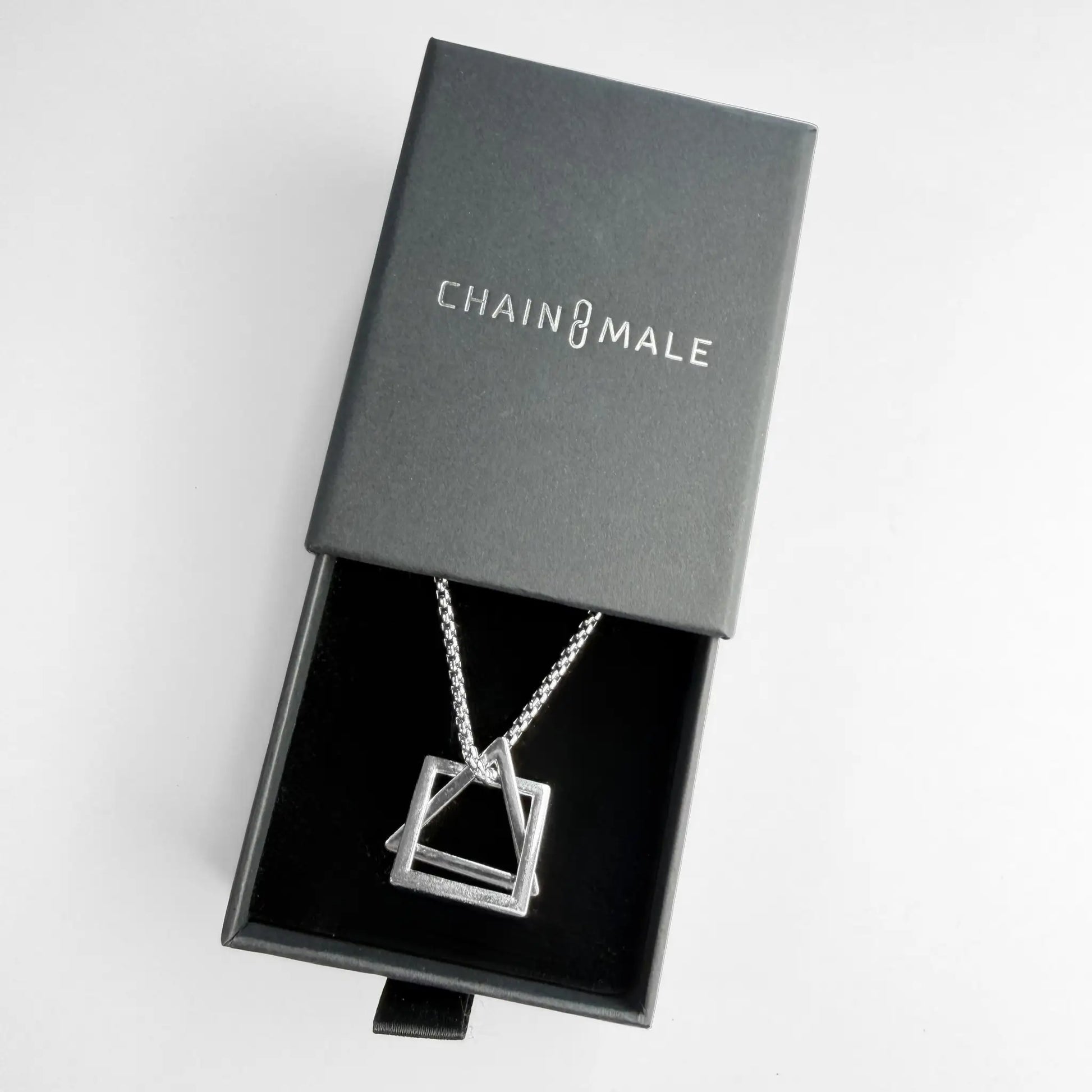 Stainless steel pendant necklace with interlocking square and triangle in a black Chain Male jewellery box on a white background