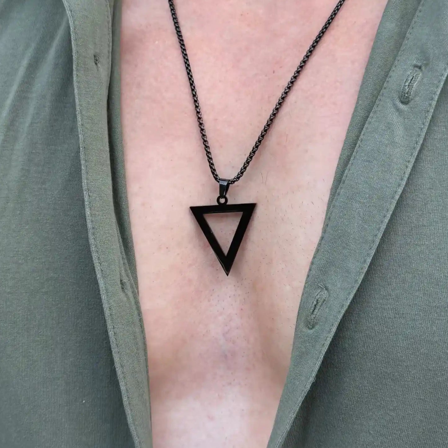Close up of a black pendant necklace worn by a man with a green button shirt