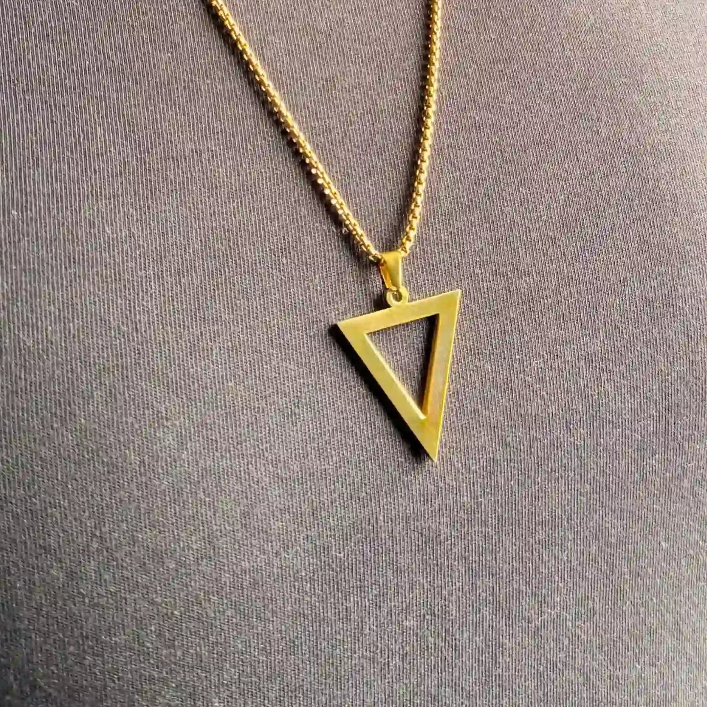 Close up of a gold triangle pendant necklace worn over a black tshirt