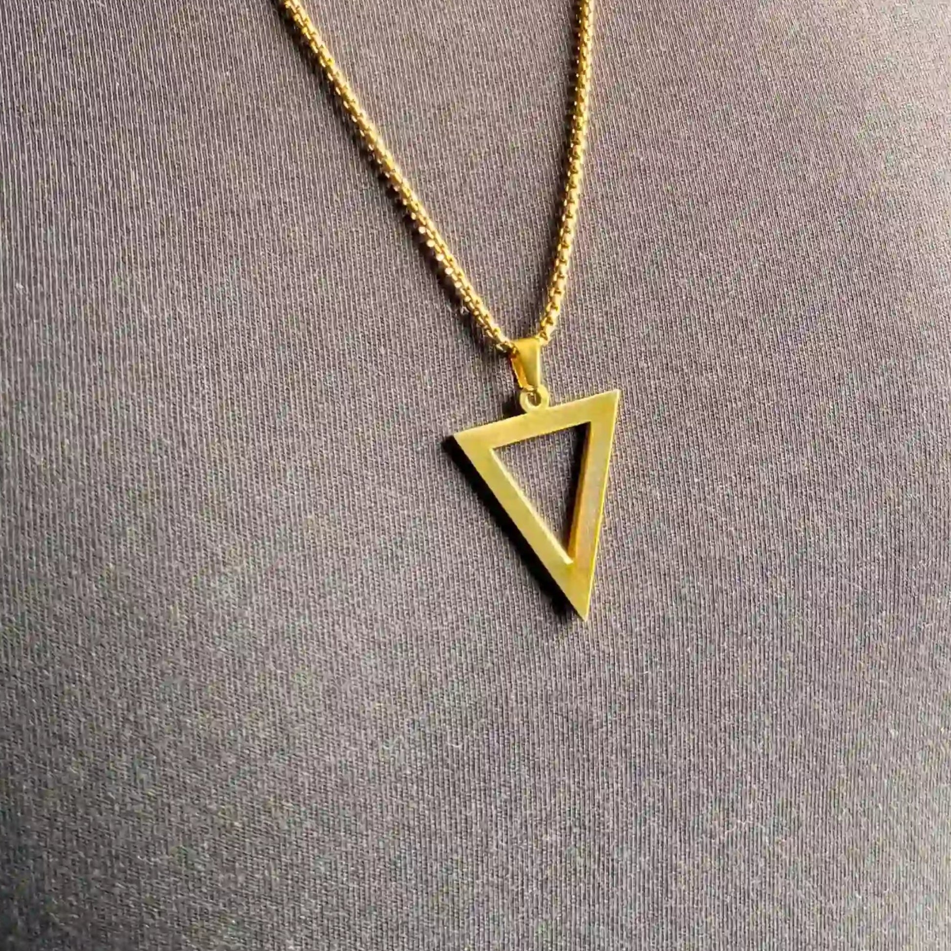Close up of a gold triangle pendant necklace worn over a black tshirt