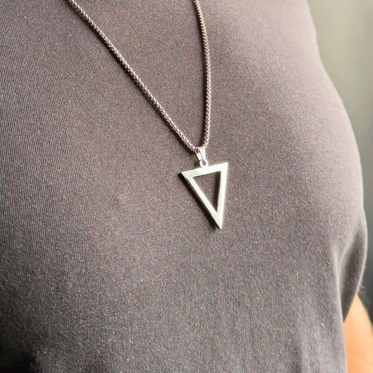 Close up of a stainless steel silver triangle pendant necklace worn by a man in a black tshirt