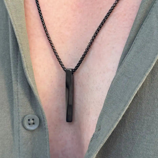 Close up of a black bar pendant necklace worn by a man in a green button shirt