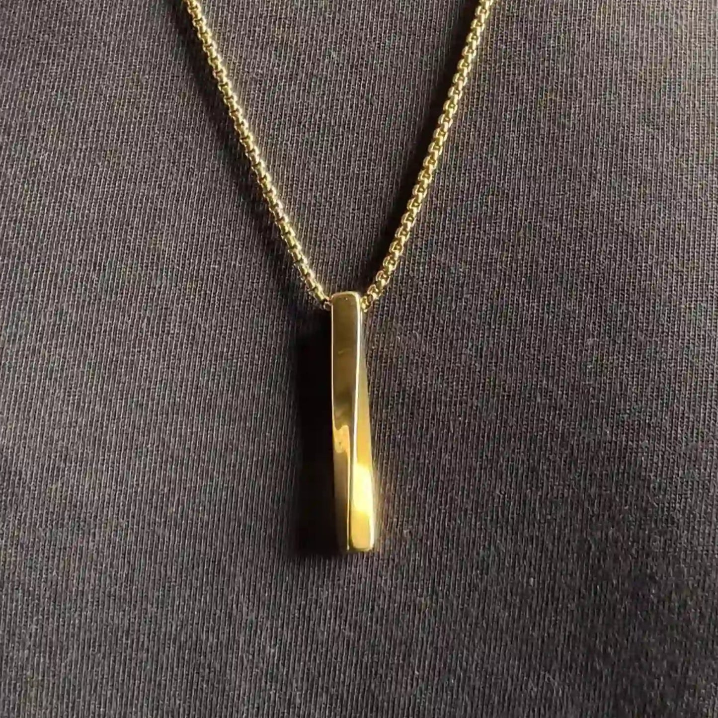 Close up of a gold plated stainless steel bar pendant necklace worn over a black tshirt