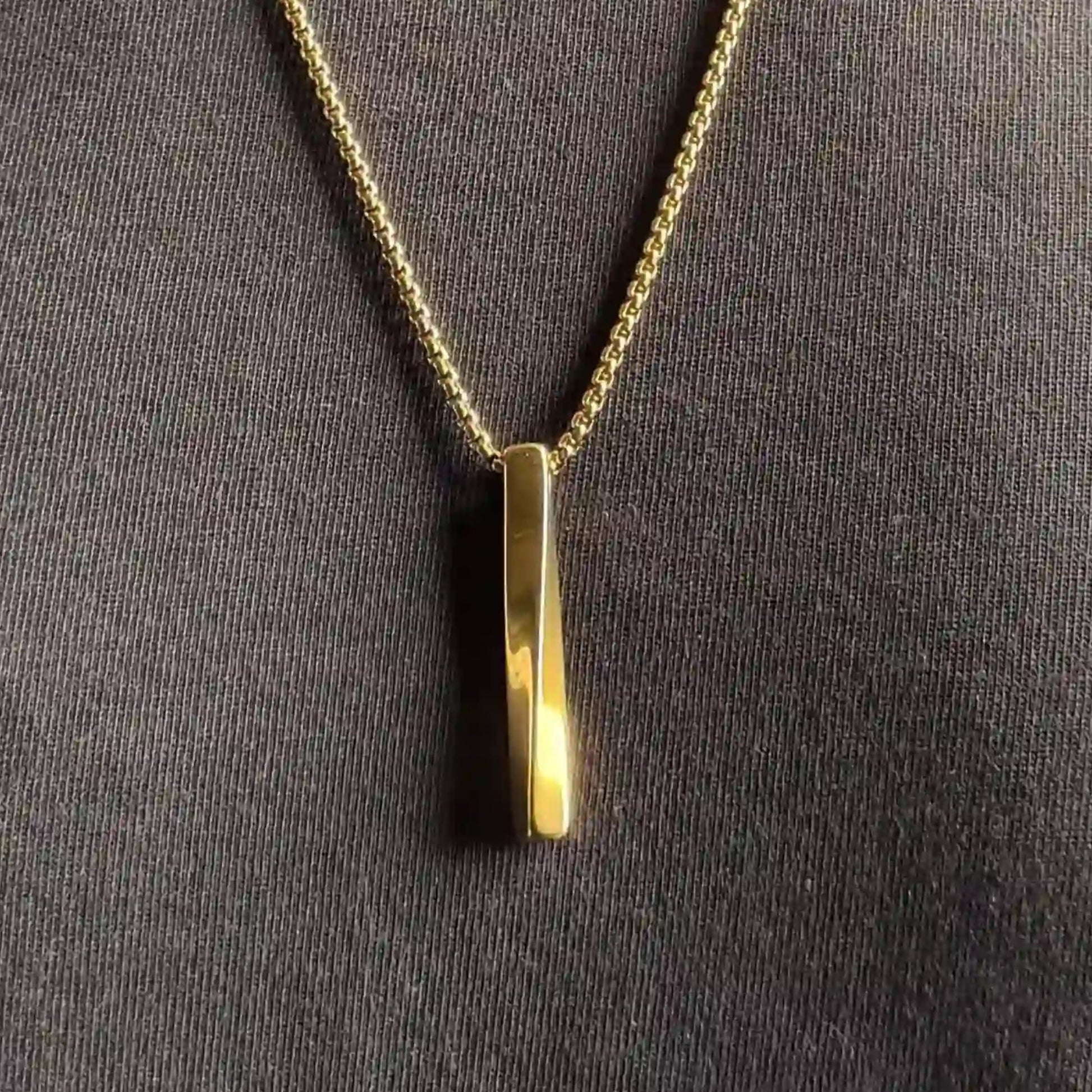 Close up of a gold plated stainless steel bar pendant necklace worn over a black tshirt