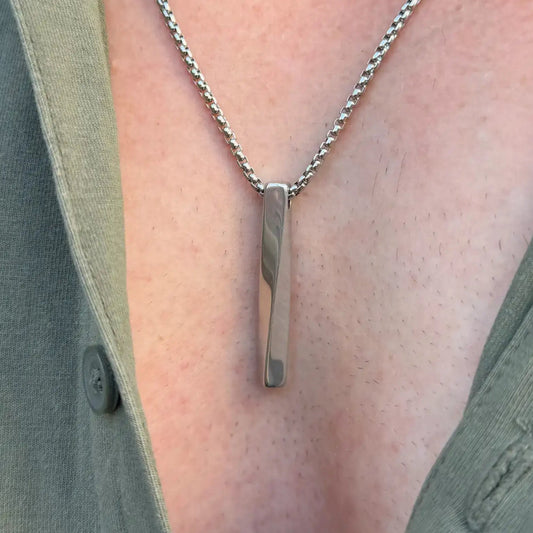 Close up of a stainless steel bar pendant necklace worn by a man with a green button shirt