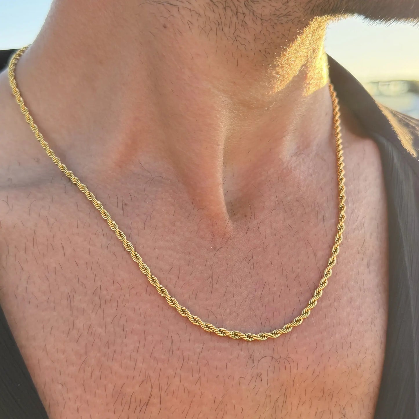 Close-up of a gold rope chain necklace worn by a man in a dark singlet at sunset