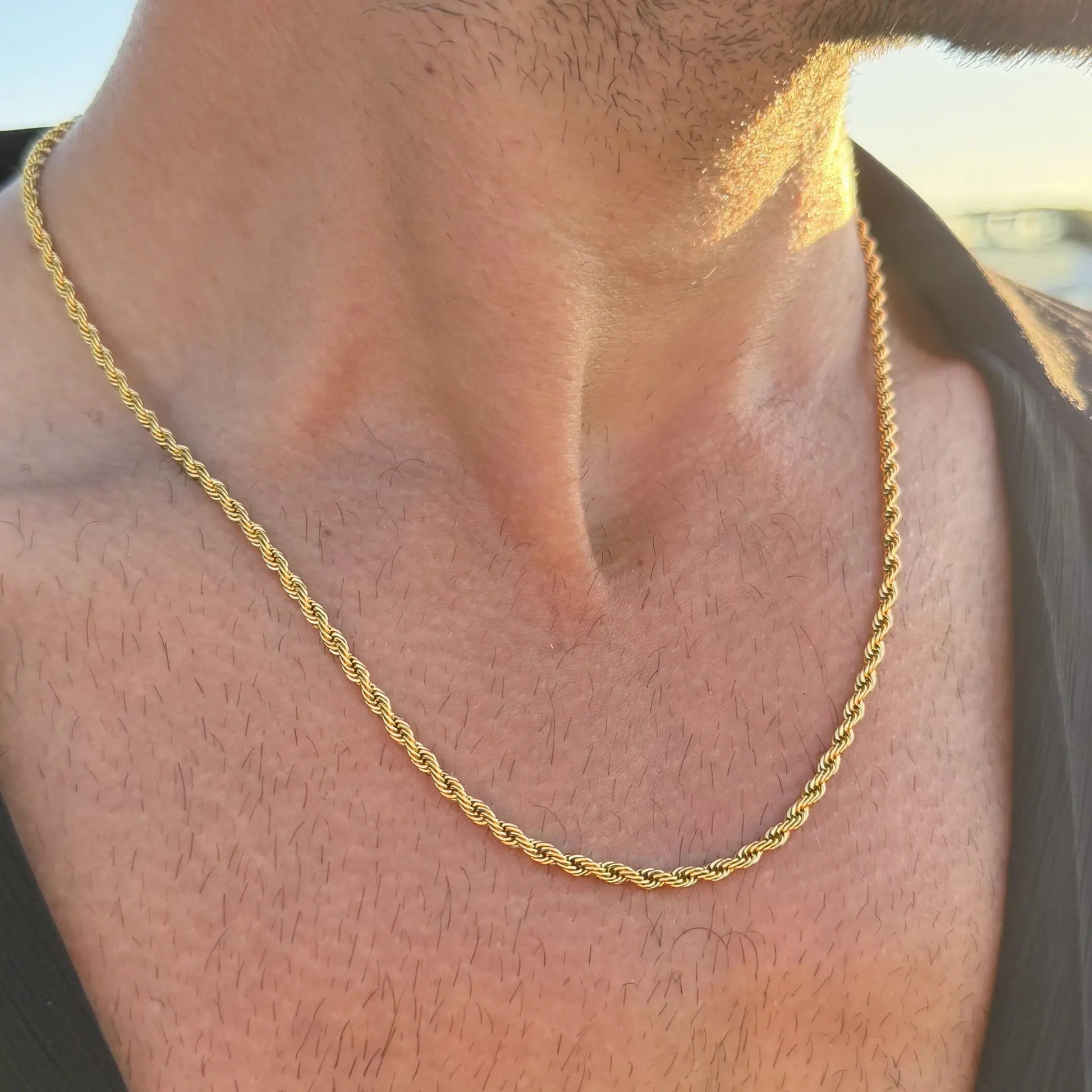 Close-up of a gold rope chain necklace worn by a man in a dark singlet at sunset