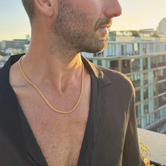 Man wearing a gold rope chain necklace outdoors at golden hour with Melbourne city skyline in background