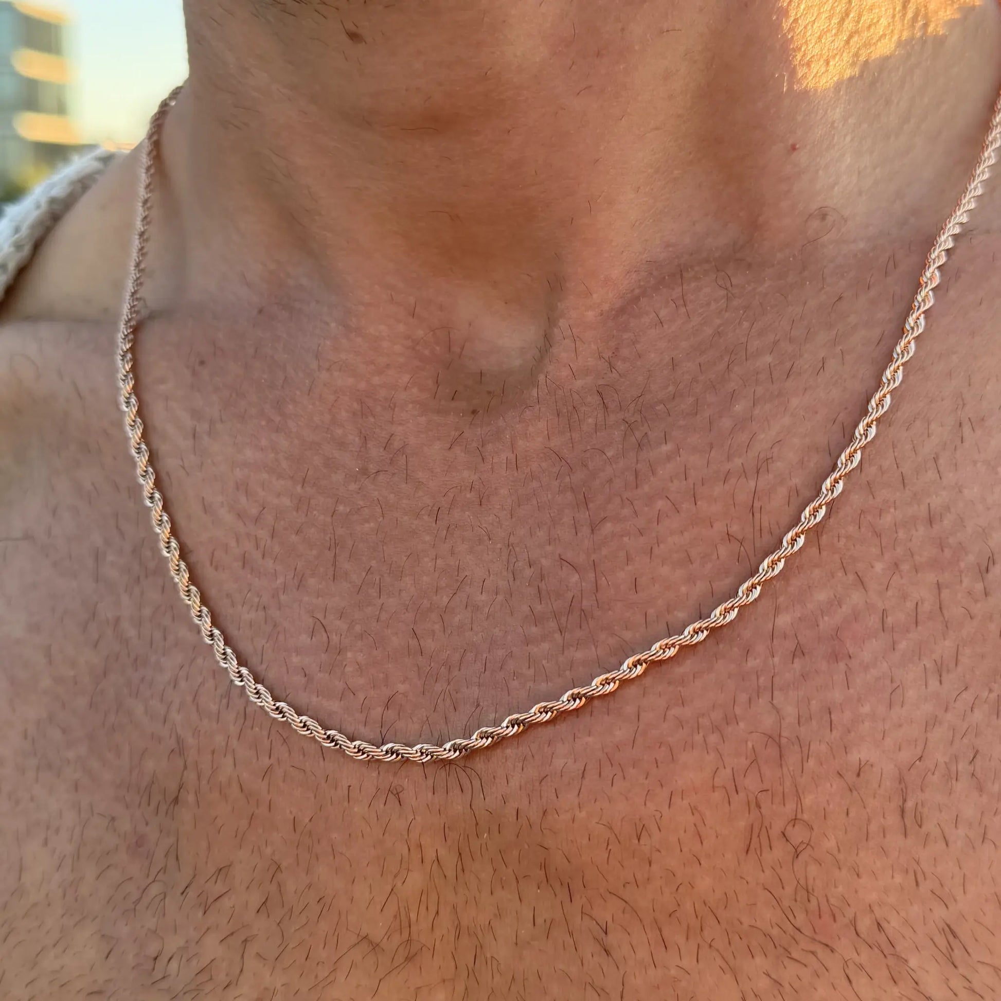 Close-up of a rose gold rope chain necklace worn on a bare chest at golden hour