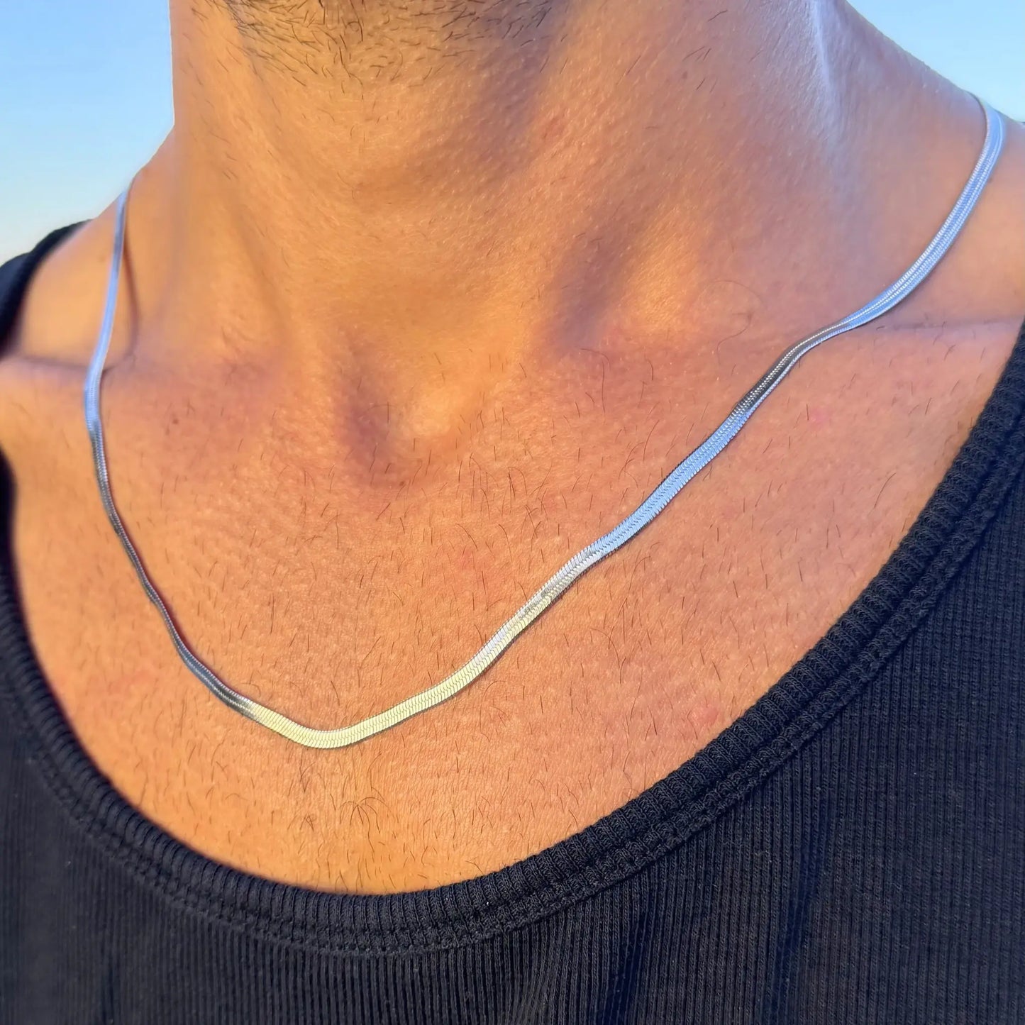Close-up of a silver 3mm snake chain necklace worn by a man in a black singlet at sunset